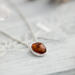  A playful 18" sterling silver necklace with a 10mm Baltic amber oval pendant on a light wood table, surrounded by soft decor. 
